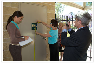 access 
consultants outdoors measuring the height of signage on disabled toilets