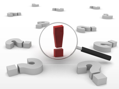 magnifying glass zooming in on an exclamation mark with question marks lying around it.